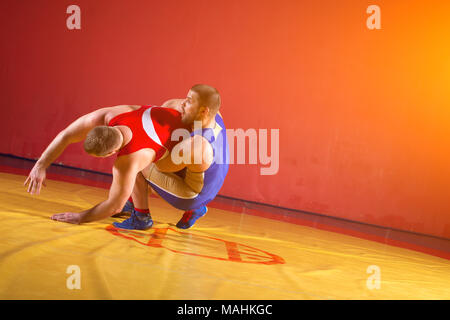 Zwei junge Mann Ringkämpfer in roten und blauen Uniform wrestling auf einem gelben wrestling Teppich in der Turnhalle. Grappling. Stockfoto