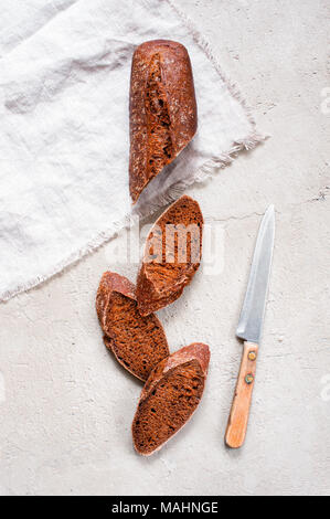 Laib Schwarzbrot und Küche Messer auf die texturierte graue Tabelle, Ansicht von oben Stockfoto