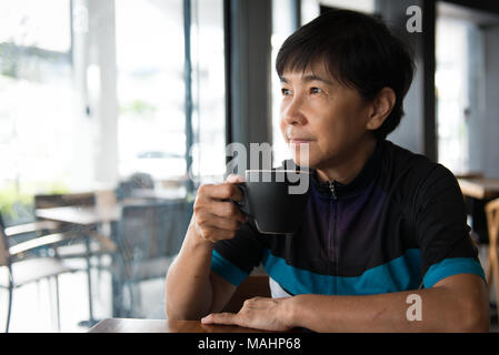 Senior asiatische Frau mit Kaffee in Trikot Stockfoto