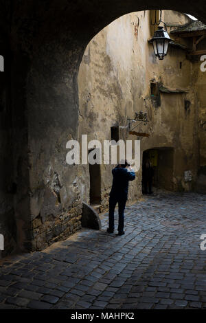 Ein Mann nimmt ein Foto auf den gepflasterten, engen und bunten Straßen Liquidation der Zitadelle in der Altstadt von Schäßburg, Siebenbürgen, Rumänien. Stockfoto