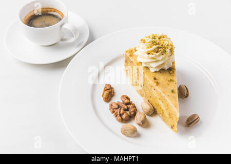 Nahaufnahme Blick auf Stück Kuchen mit Muttern und Tasse Kaffee isoliert auf weißem Stockfoto