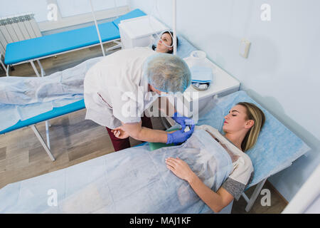 Krankenschwester macht eine Injektion mit einer Frau am OP-Tisch am Klinikum Vorbereitung Narkose medizinische Arztpraxis Konzept liegen. Stockfoto