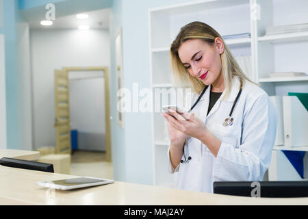 Lächelnd weibliche Arzt tragen eine Bereinigung und Arbeiten im Krankenhaus, Rezeption, sie schreibt einen medizinischen Bericht über eine Zwischenablage und Planen von Terminen Stockfoto