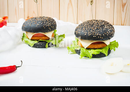 Schwarz Burger mit Hühnerschnitzel, Käse, Tomaten und Salat serviert auf weißem Holz Hintergrund. Stockfoto