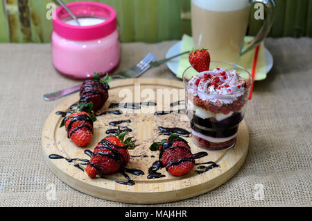 Dessert trifle mit Heidelbeere Sahne und Erdbeeren auf einem Hintergrund von sackleinen und Kaffee Latte mit Zucker im Hintergrund Stockfoto