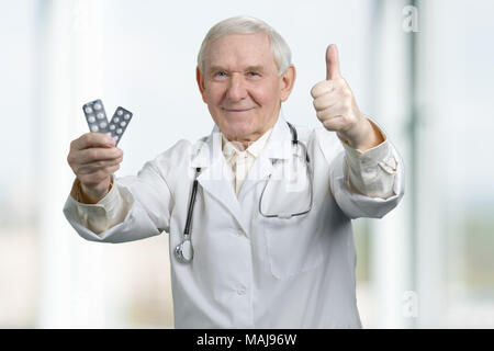 Leitender Therapeut mit zwei Packs der Medizin. Porträt eines überzeugten alten männlichen Arzt mit Stethoskop in Uniform holding Pillen Packung und showin gekleidet Stockfoto