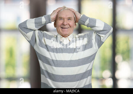 Älterer Mann seinen Kopf berühren schockiert. Portrait von alten Großvater in Windows Hintergrund. Stockfoto