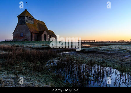 Der hl. Thomas Becket Kirche in die Sümpfe. Winter Dawn Twilight, Frost auf den Boden, halb gefrorenen Graben mit Schilf, Kirche am Horizont. Romney Marsh, Großbritannien. Stockfoto