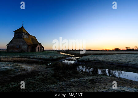 Der hl. Thomas Becket Kirche in die Sümpfe. Sunrise, Frost auf den Boden, halb gefrorenen Graben mit Schilf, Kirche am Horizont. Romney Marsh, Großbritannien Stockfoto