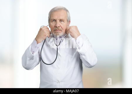 Leitender Chirurg setzen auf ein Stethoskop. Porträt von Ernst Arzt tragen Stethoskop. Helle verschwommenen Hintergrund. Stockfoto