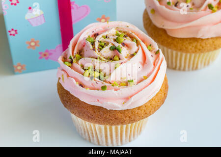 Zwei peach rose Frosted Cup Cakes mit Pistazie wirbelte Streusel auf weißem Hintergrund mit Platz für Ihren Text Stockfoto