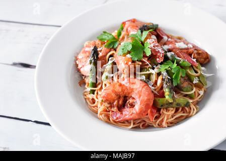 Spaghetti Frutti di Mare oder Pasta mit Garnelen und grünem Spargel und Petersilie garnieren. Weiße Platte auf einem Holztisch, gesunde Ernährung Szene. Stockfoto