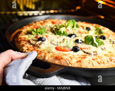 Hausgemachte Pizza. Vegetarische Pizza im Pizza pan, Gemüse Pizza mit Brokkoli, Champignons, Tomaten und Oliven. Pizzabacken Szene. Stockfoto