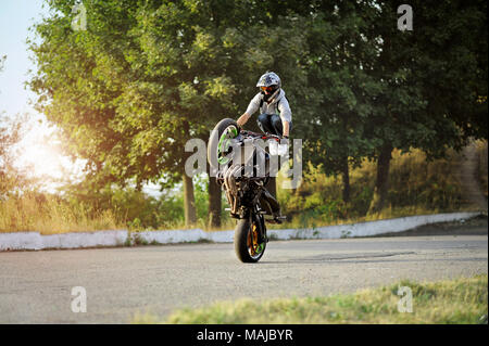 Ternopil, Ukraine - 28. August 2015: Männlich Biker ist Ausbildung in die Tricks auf Sport Motorrad auf Sommer zitieren Straße. Grüne Bäume im Hintergrund. Das Tragen von Helm. Stockfoto