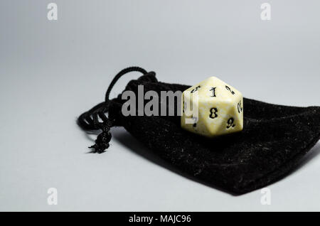 Weißer 20-seitige Würfel auf eine kleine schwarze Handtasche auf einem weißen Hintergrund. Würfel von Rollenspiel Stockfoto