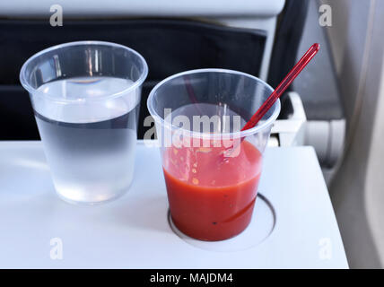 Mit dem Flugzeug reisen, Flug Service. Zwei Getränke auf einem Flugzeugsitz Tabelle. Kunststoff Gläser mit Wasser und Tomatensaft. Stockfoto