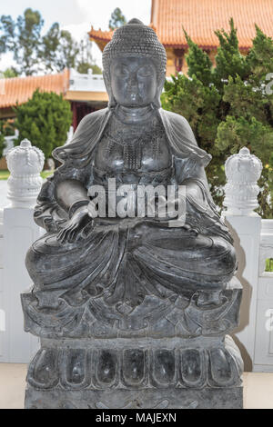 Hacienda Heights, CA, USA - 23. März 2018: Dunkelgrau Granit Statue der Erleuchtung des Buddha auf Seite der Garten mit Lotus Podest Hsi Stockfoto