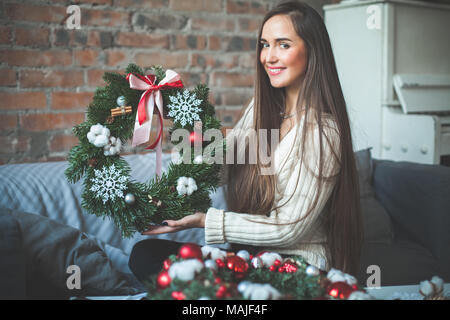 Junge hübsche Frau Florist mit Weihnachtsbaum Kranz mit roten Kugeln aus Glas, Farbband und Weiße Schneeflocke Stockfoto