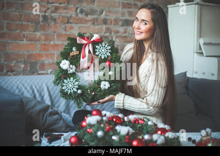 Junge hübsche Frau mit Weihnachten immergrüner Baum Kranz mit roten Kugeln aus Glas, Kegel, Farbband und Zimt zu Hause Stockfoto