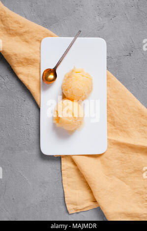 Zwei Bälle von zitronensorbet in die weiße Platte auf gelb serviette, strukturierte graue Tabelle. Ansicht von oben Stockfoto