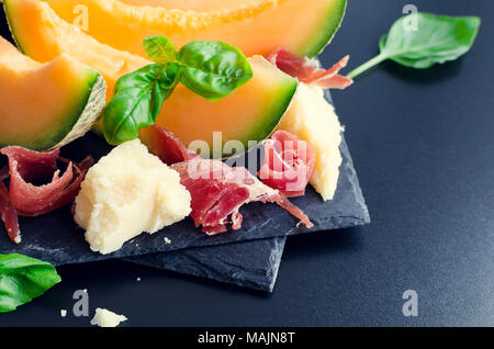 Konzept der italienische Küche mit Melone und Schinken auf dunklem Hintergrund. Traditionelle Vorspeise Antipasto. Selektive konzentrieren. Stockfoto