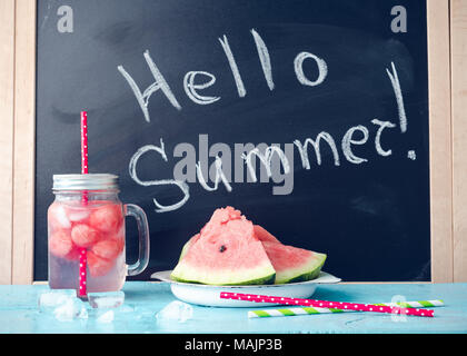 Hallo Sommer auf der Tafel mit Getränk im Glas Marmeladenglas mit Scheiben von Wassermelone und Eis auf blauem Hintergrund geschrieben. Frisches Obst aromatisierte hineingießen Stockfoto