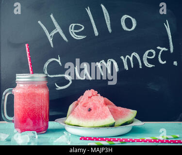 Hallo Sommer auf der Tafel mit Wassermelone Saft im Glas Marmeladenglas mit Scheiben von Wassermelone und Eis auf blauem Hintergrund geschrieben. Frisches Obst flav Stockfoto