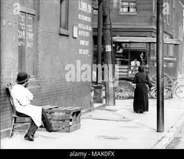 Horizontal, Schwarz und Weiß Foto, eine jüdische Metzgerei außerhalb seiner Store auf North St. Louis Seite sitzen, wahrscheinlich Franklin Avenue. Der Mann sitzt auf einem Stuhl auf der linken Seite des Bildes, unter einem Fenster mit hebräischen Schrift. Ein Zeichen für "A. Cohen & Sohn' ist an der Ecke des Gebäudes gemalt. Eine Frau auf dem Bürgersteig auf der rechten Seite des Bildes, und ein Wagen ist das Fahren auf der Straße. Eine handschriftliche Notiz auf der Rückseite des Drucks, wahrscheinlich aus der Schulschwestern, liest: "A. Cohen & Sohn Immo (1910)/919 Waschen / 1934 Franklin (1916)." Titel: Jüdische butc Stockfoto