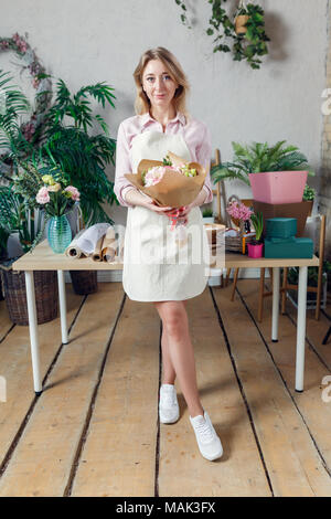 Foto der jungen Frau Blumenhändler in Schürze mit Blumenstrauß in den Händen Stockfoto
