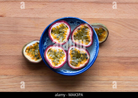 Saftig und lecker Passionsfrucht, in Scheiben geschnitten und in eine handgefertigte Keramik Schüssel mit Holz- Hintergrund angezeigt. Stockfoto