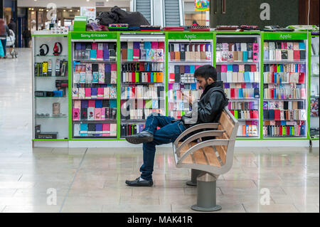 Handy Cover mit Mann sitzt auf der Bank mit einem Mobiltelefon im Lower Precinct, Coventry, West Midlands, UK. Stockfoto