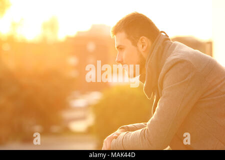 Seitenansicht Portrait von ein ernster Mann entfernt auf einem Balkon mit Blick auf den Sonnenuntergang im Winter Stockfoto