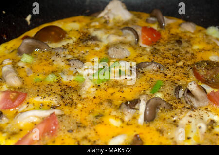 Kochen ein Omelett Omelett close-up Kochen in Gusseisen Skillet mit Pilzen, Tomaten und Frühlingszwiebel und mit schwarzem Pfeffer garniert Stockfoto
