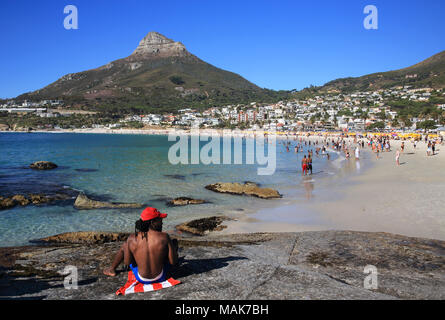 Schwarzer Mann sitzen auf dem Felsen von den feinsandigen, weißen Strände von Luxushotels in Camps Bay, mit Löwenkopf, Jenseits, in Kapstadt, Südafrika Stockfoto