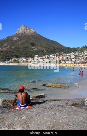 Schwarzer Mann sitzen auf dem Felsen von den feinsandigen, weißen Strände von Luxushotels in Camps Bay, mit Löwenkopf, Jenseits, in Kapstadt, Südafrika Stockfoto