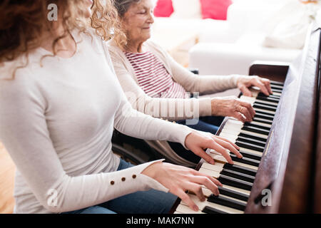 Ein Mädchen mit Großmutter im Rollstuhl Klavier spielen. Stockfoto