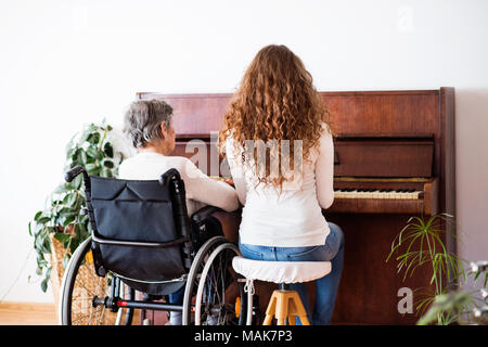 Ein Mädchen mit Großmutter im Rollstuhl Klavier spielen. Stockfoto