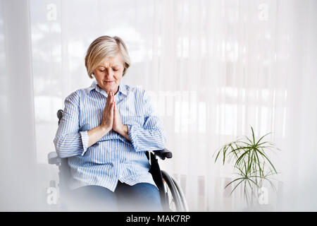 Eine ältere Frau im Rollstuhl zu Hause beten. Stockfoto