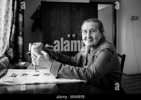 Süße 80 Jährige ältere Frau mit Vintage Nähmaschine. Schwarz-weiß Bild von adorable ältere Frau nähen Kleidung in ihrer alten Familie zu Hause. Stockfoto