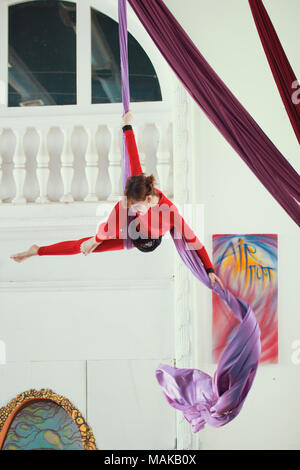 Weibliche Luft Gymnast in einem roten Sportswear führt eine Übung auf Antenne Seide Stockfoto