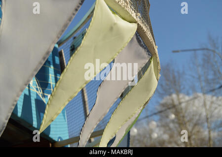 Close-up, selektiver Fokus, Wind klatscht Girlanden aus bunten Fahnen gegen den blauen Himmel, Park im Frühling Stockfoto