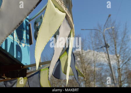 Close-up, selektiver Fokus, Wind klatscht Girlanden aus bunten Fahnen gegen den blauen Himmel, Park im Frühling Stockfoto