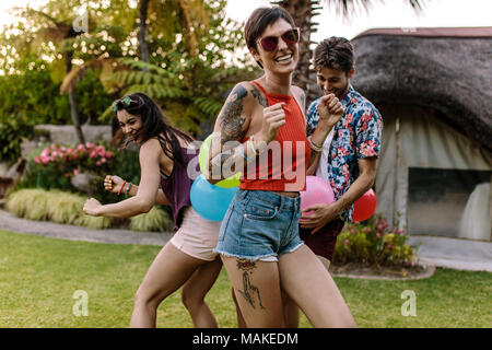 Glückliche junge Frau genießen Sie auf einer Party mit Freunden spielen Balloon popping Spiel im Hintergrund. Menschen Spaß an Summer Party. Stockfoto