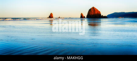 Blaue Stunde verschmilzt mit der Goldenen Stunde in diesem simplic Szene von Cannon Beach, Oregon, zwei ikonische Gezeiten Felsen, Nadeln und Heuhaufen. Ich liebe early Morn Stockfoto