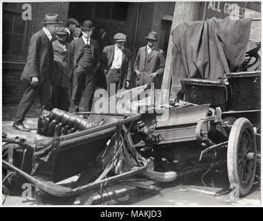 Horizontal, schwarz-weiß Foto mit einer ruinierten Auto nach einem Unfall. Das Heck des Wagens ist verzogen und zerfleischt, und ein Rad ist horizontal unter der Karosserie des Autos. Zwei Sitze von der Kamera entfernt. Sie haben abgesehen wurde bei dem Unfall zerrissen, und ein Sitz ist leicht nach hinten gelehnt. Auf der linken Seite des Bildes, zwei Männer stehen auf dem Bürgersteig am Auto suchen. Auf der rechten Seite des Bildes, ein Pferd ist, einem unsichtbaren Fahrzeug genutzt. Für ein Detail des Autos, siehe Bild Nummer P 0054-00017. Titel: Masse auf einer ruinierten Automobil. . Ca. 1908. Holt Stockfoto