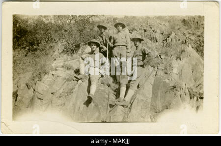 Horizontale, sepia Foto, vier uniformierte Männer stehen und sitzen auf einem felsigen Hügel für ein Gruppenfoto posieren. Titel: Vier Soldaten für ein Gruppenbild auf einem felsigen Hügel posieren. . Zwischen ca. 1916 und ca. 1918. Stockfoto