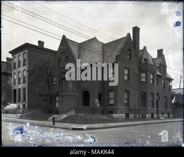 Horizontal, schwarz-weiß Foto zeigt eine ausgedehnte Backsteinhaus auf einem nicht identifizierten Straße Ecke. Eine schmale, dreistöckiges Haus ist auf der linken Seite, und eine Straße mit Kopfsteinpflaster läuft durch den Vordergrund. Titel: Häuser auf einer unbekannten Ecke. . Zwischen 1900 und 1920. Stockfoto