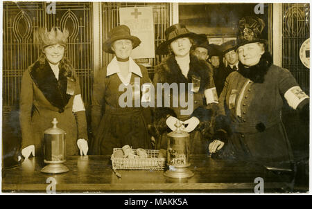 Horizontale, sepia Foto, vier Frauen, die das Tragen der Roten Kreuz Armbinden hinter einem Tisch, mit Sammlung Dosen für ein Krankenhaus auf dem Tisch. Drei andere Personen können im Hintergrund des Bildes zu sehen. Titel: Vier Frauen sammeln Geld für das Rote Kreuz. . 1917. Michel, Carl Stockfoto