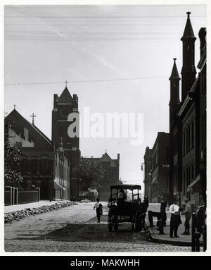 Vertikal, schwarz-weiß Foto eines Street View des Vierzehnten und Franklin Straßen. Ein Mann in der Mitte der Ziegel gepflasterte Straße und ein Pferdefuhrwerk auf der rechten Seite der Straße geparkt. Zwei Männer stehen an der Ecke und auf jeder Seite der Straße ist mit gemauerten Gebäuden gesäumt. Eine Kirche ist an der Ecke von der linken Seite der Straße in der Ferne. Titel: Vierzehnte und Franklin nach Norden. . 1909. Swekosky, William G., 1895-1964 Stockfoto