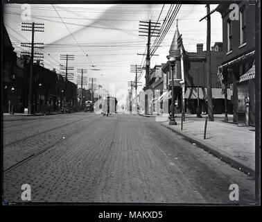 Horizontal, schwarz-weiß Foto zeigt den Blick hinunter die Straße an der Kreuzung von Taylor und Easton. Easton wurde später umbenannt in Dr. Martin Luther King. Eine Vielzahl von Geschäften und Unternehmen sind im zwei-stöckige Gebäude, die beiden Seiten der gepflasterten Straße untergebracht. Straßenbahn Titel Run auf der Mitte der Straße, und eine Straßenbahn im Hintergrund gesehen werden. Es gibt auch mehrere Autos und Fußgänger. Ein Hinweis an der oberen Kante an der Rückseite des negativen liest: "406-9702/Taylor und Easton." Titel: Blick nach unten auf der Straße an der Kreuzung o Stockfoto